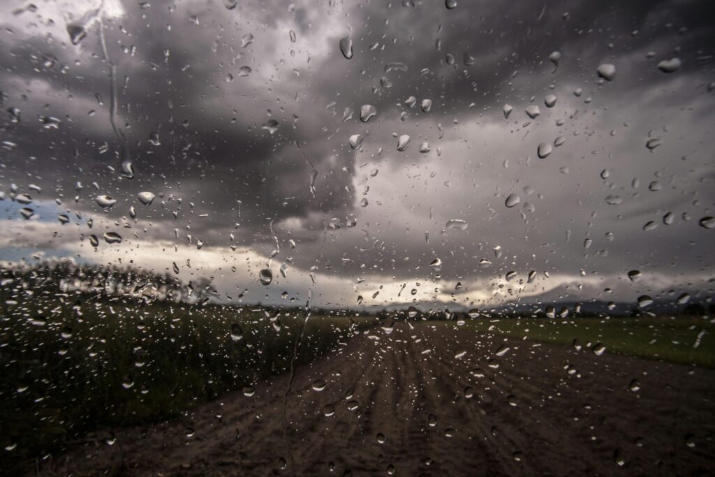A scenic view of raindrops on glass with a cloudy field background, creating a dramatic effect.