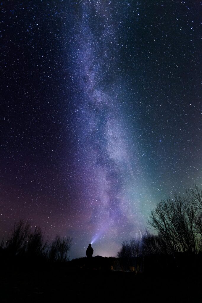 A breathtaking view of the Milky Way above a silhouetted figure exploring the night sky.