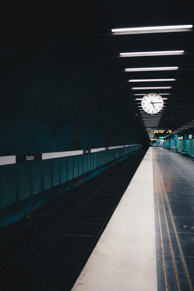 A moody view of an empty subway station in Stockholm with a large clock on the ceiling.