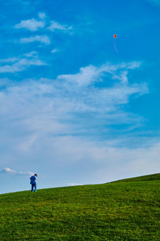 DAY 54 - DISCOURAGED? A young boy in a blue shirt flies a red kite on a sunny day in a wide open grass field.