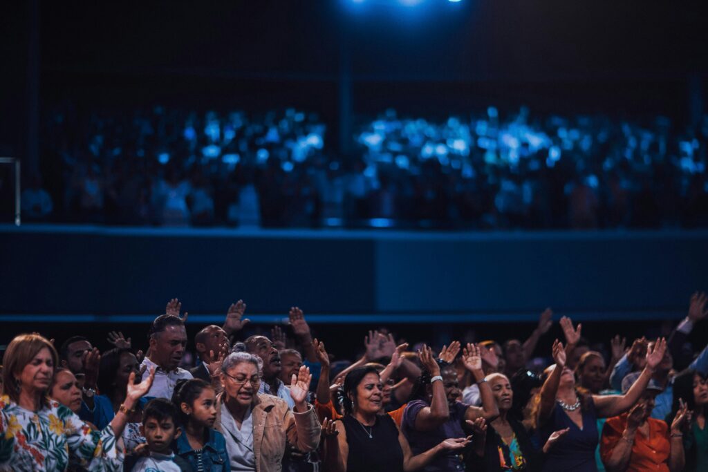 A diverse group of people raising hands in a worship setting, captured indoors.