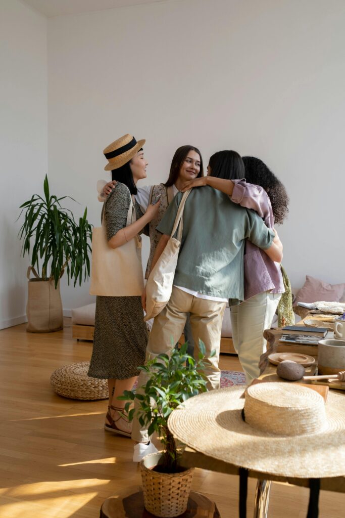 Four diverse women in casual clothes sharing a warm embrace in a cozy indoor setting.