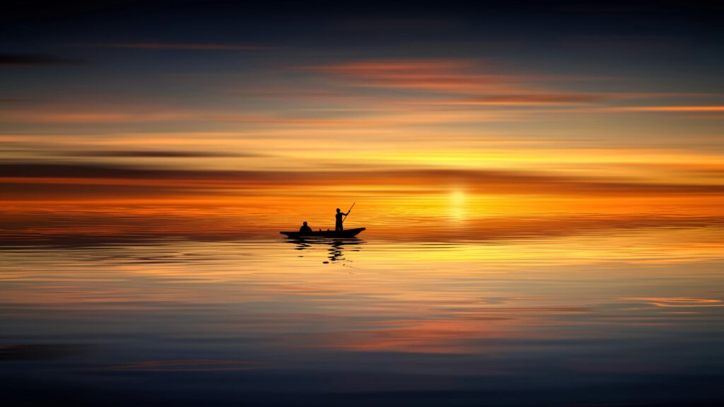 Silhouette of two people in a boat against a vibrant sunset over calm waters. Tranquil scene.