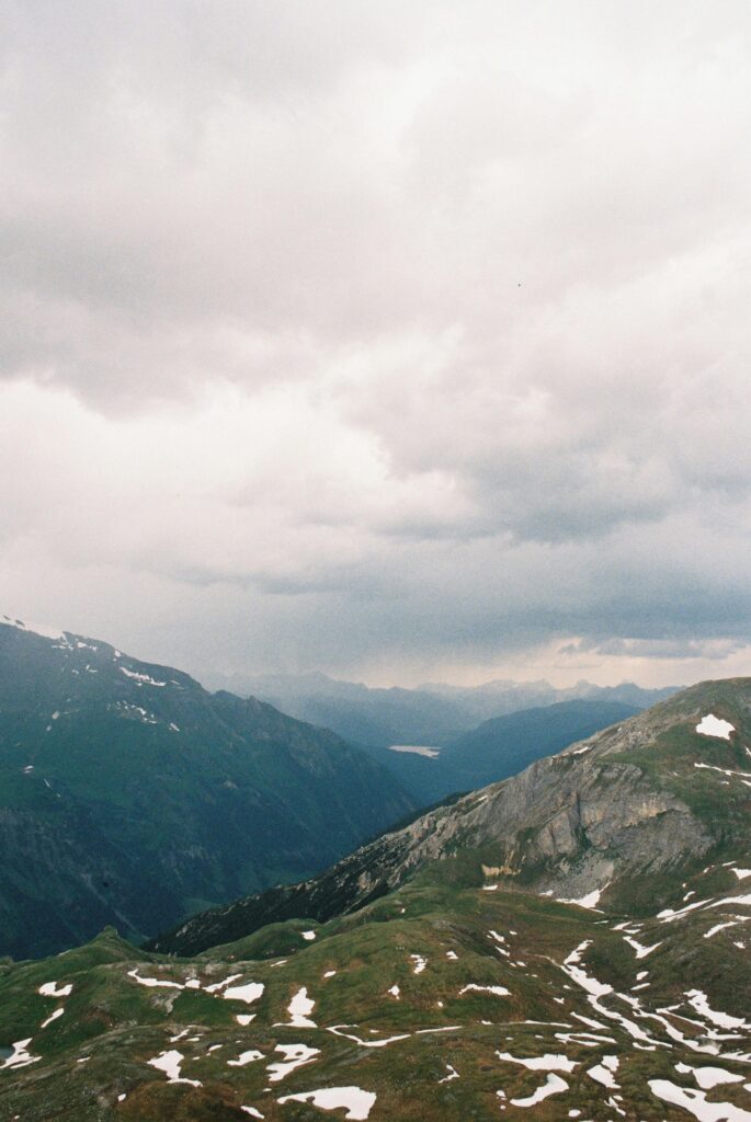 Stunning view of the Austrian Alps under a cloudy sky, showcasing rugged terrain and snow patches.