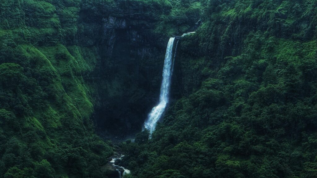 Breathtaking waterfall pouring into a verdant, green valley amidst rugged cliffs.