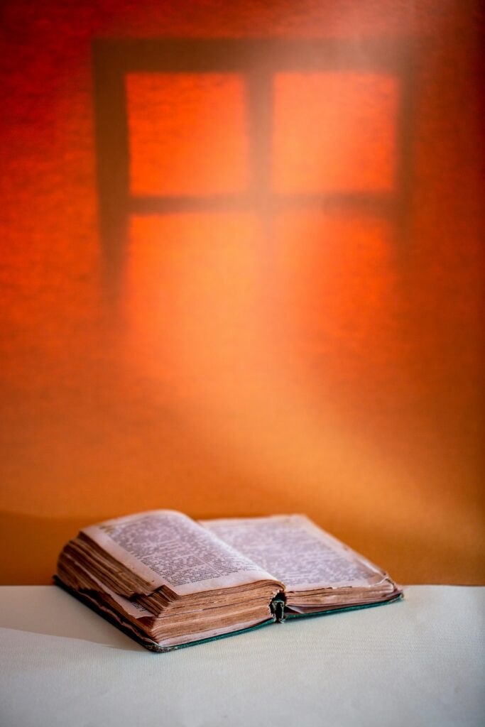 Vintage open book on table against an orange-lit wall, evoking a warm and nostalgic atmosphere.