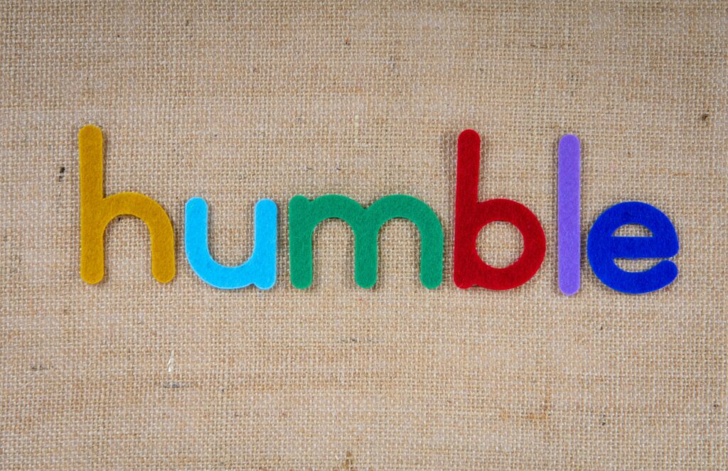 Bright colorful felt letters spelling 'humble' on burlap fabric background.