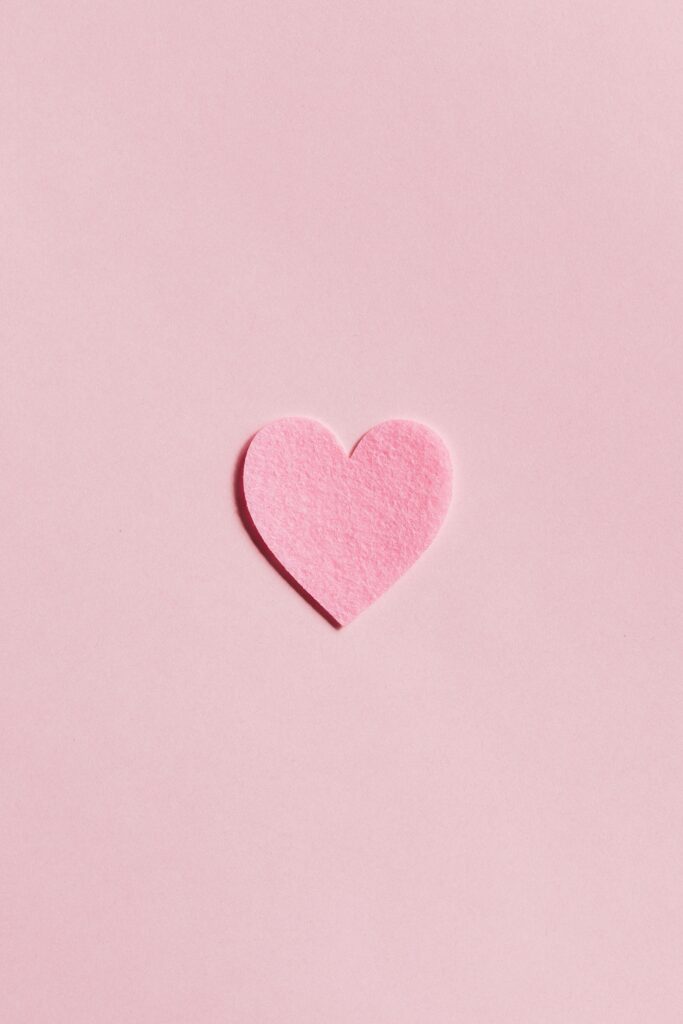 A simple pink felt heart on a light pink background, perfect for Valentine's Day themes.