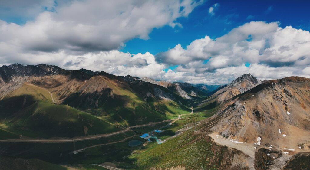 Stunning aerial view of a lush mountain valley with scenic roadways amidst dramatic skies.