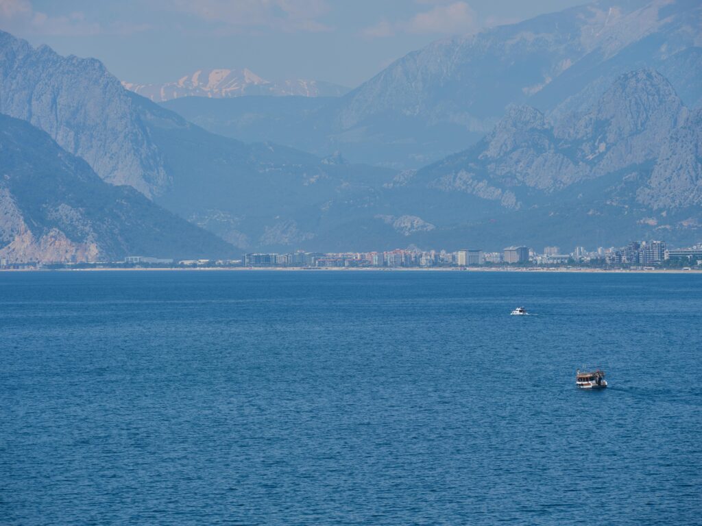 A peaceful seascape with distant mountains and boats on a clear day.