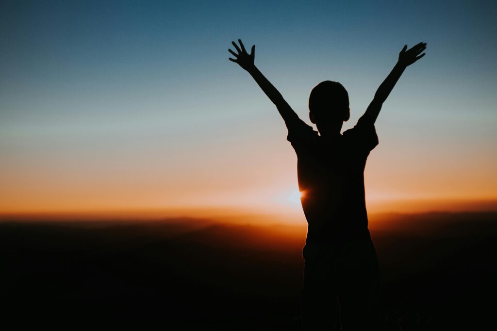 Silhouette of a child with raised arms against a vibrant sunset, evoking freedom and joy.