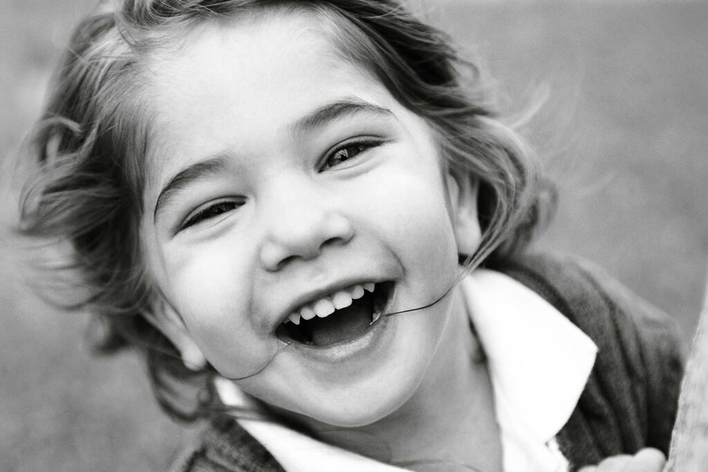 Black and white portrait of a happy child laughing outdoors. Captures pure joy and innocence.