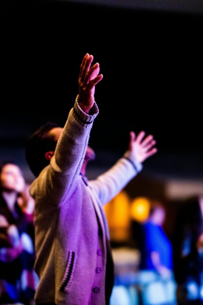 A person with arms raised in spiritual worship during an indoor event.
