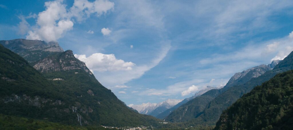 Scenic view of a lush valley framed by majestic mountains under a vibrant blue sky.