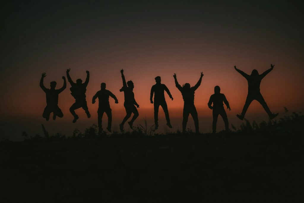 Silhouette of a group of people jumping in joy against a vibrant sunset sky.