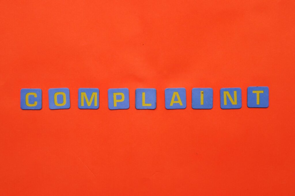 Blue letter tiles spelling 'COMPLAINT' on a vibrant red surface.