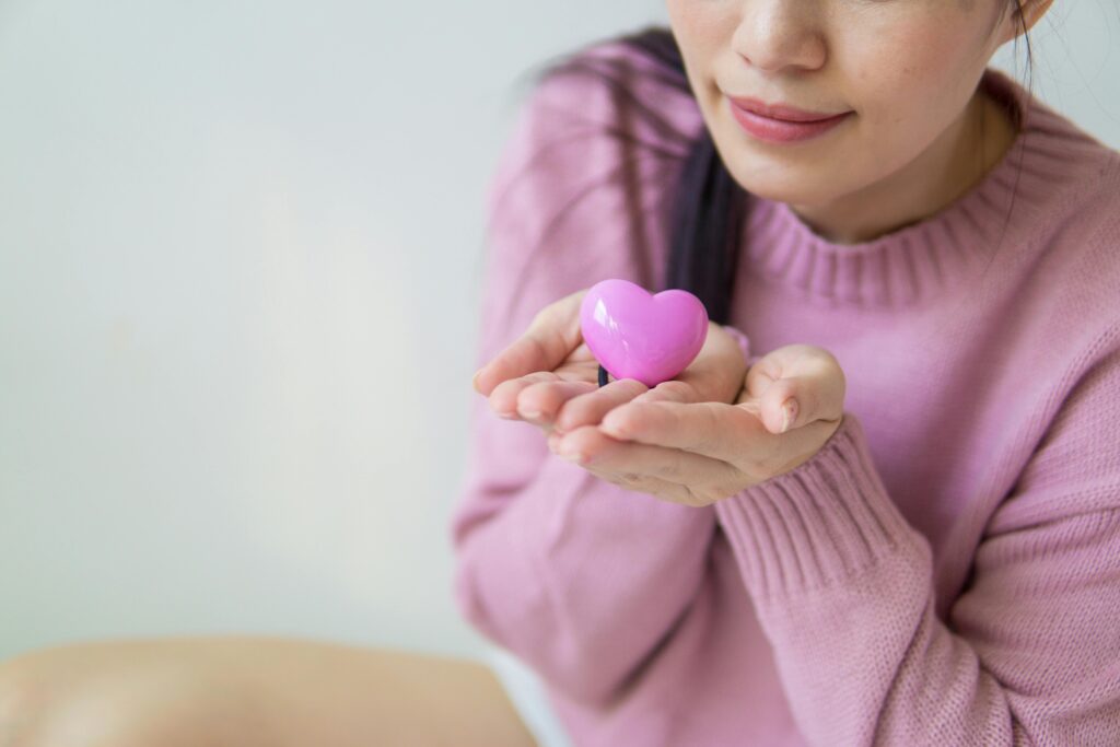 A woman in a pink sweater holding a pink heart-shaped toy, symbolizing love and kindness.
