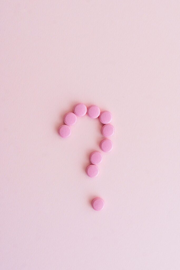 Pink pills forming a question mark on a pastel surface, symbolizing uncertainty in health decisions.