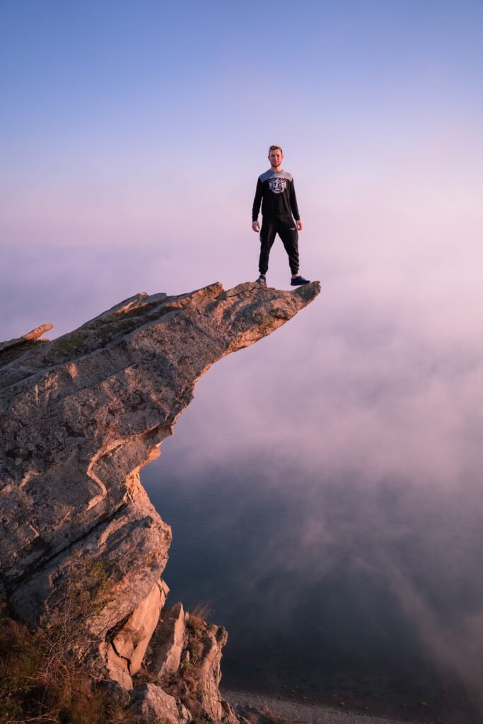 A daring adventurer stands on a cliff's edge, embracing the breathtaking sunrise view.