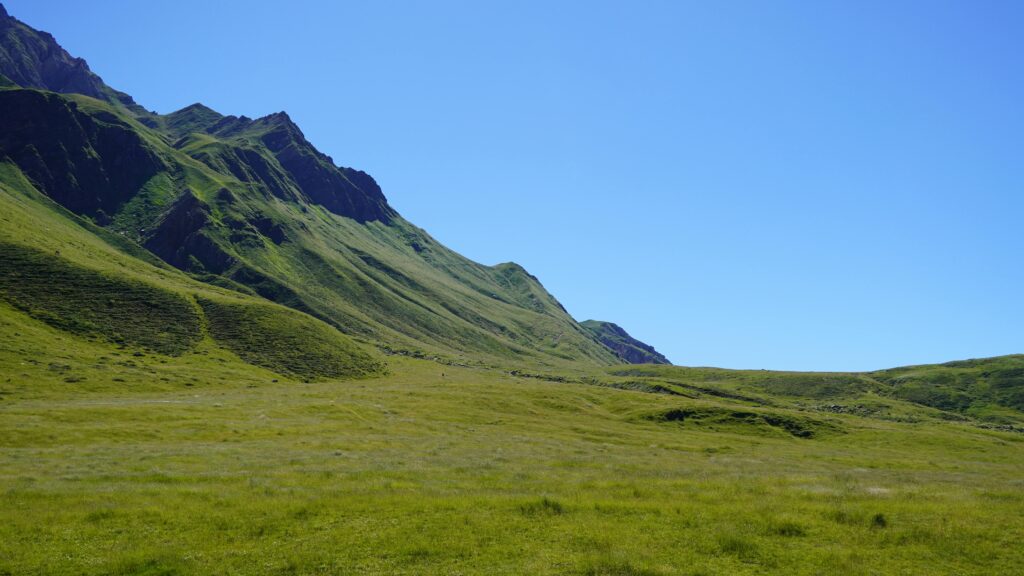 A serene landscape of a lush green valley under a bright blue sky, with mountain slopes enhancing the natural beauty.