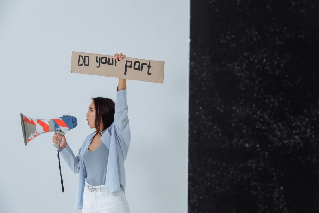 Woman holding a sign and megaphone in a studio setting, encouraging action.