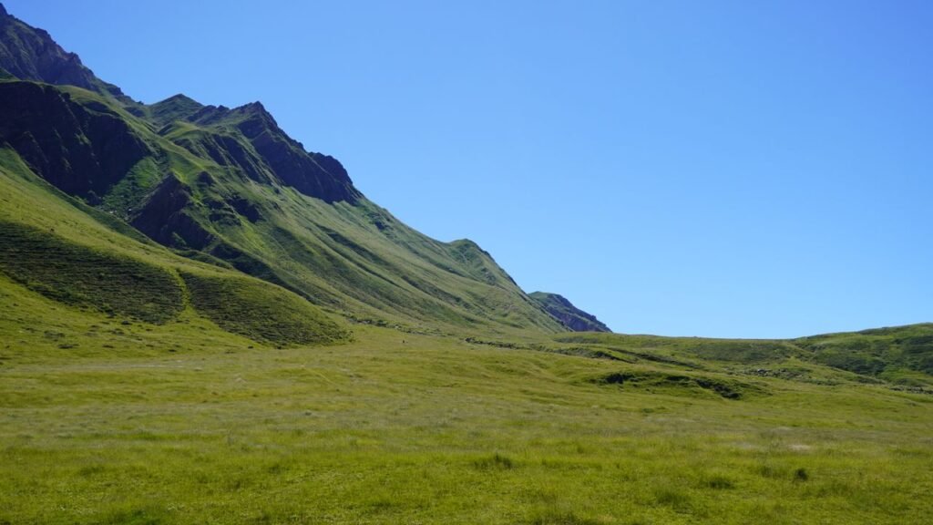 A serene landscape of a lush green valley under a bright blue sky, with mountain slopes enhancing the natural beauty.