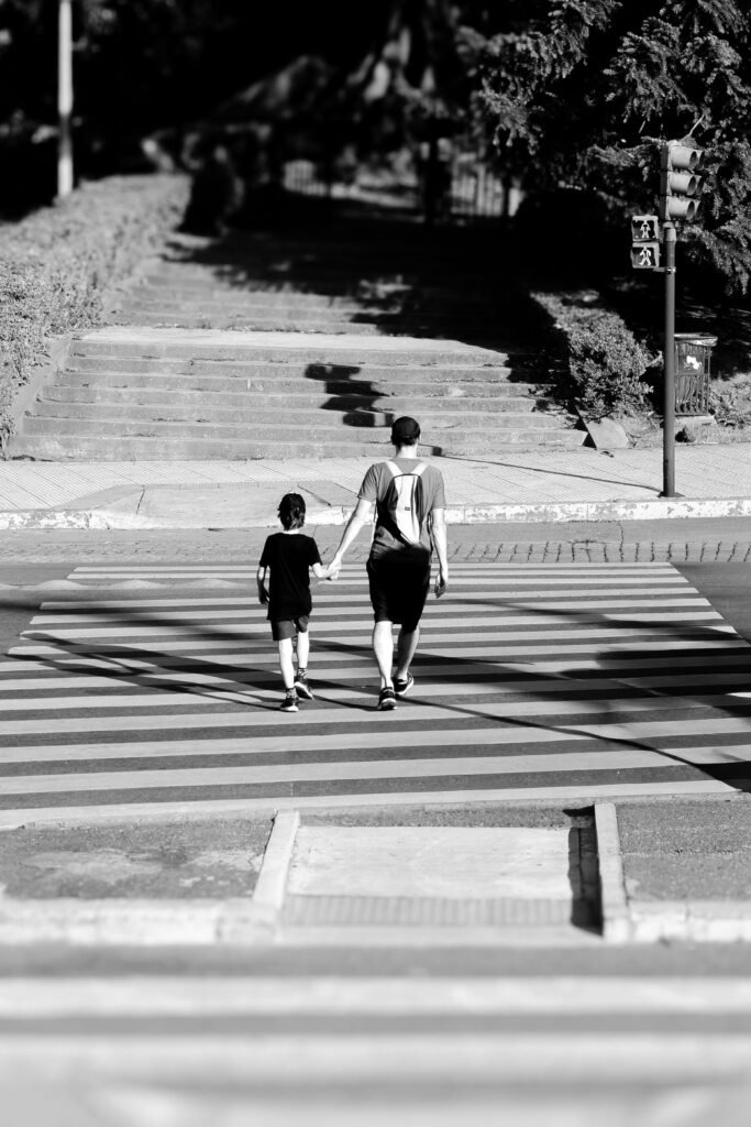 Monochrome image of a father and child crossing a street holding hands, showcasing bonding and safety.