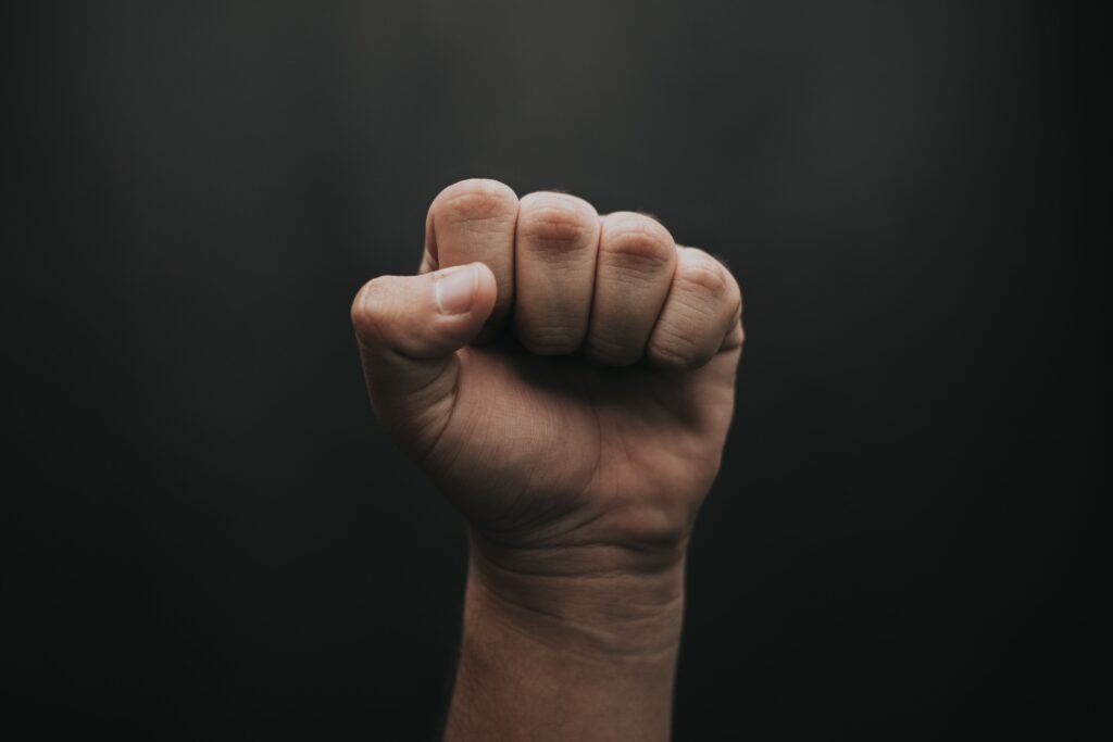 3 OCTOBER 2026, DAY 276 - STRENGTH IN YOUR WEAKNESS A close-up of a fist raised against a dark background, symbolizing strength and unity.