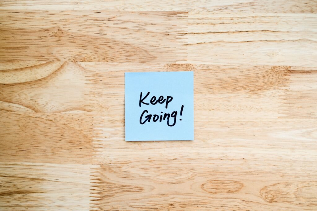 A blue sticky note with 'Keep Going!' message on wood background.