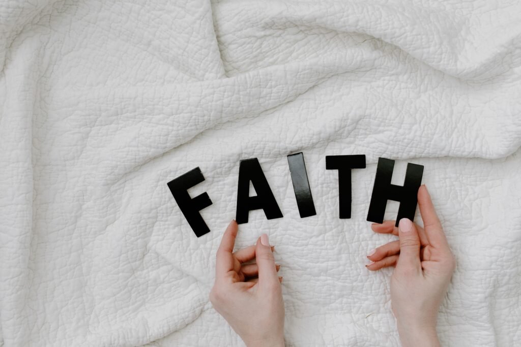 Hands arranging letters on a white quilt spelling FAITH. Minimal and serene concept.